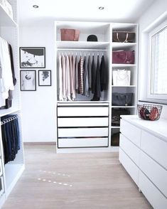 a white closet filled with lots of clothes next to a dresser and drawers in front of a window