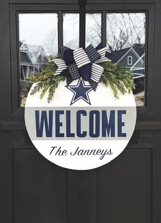 a welcome sign hanging on the front door of a house with wreaths and bows