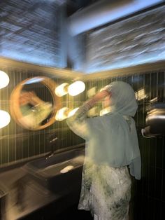 a woman standing in front of a mirror with lights on her head and hands behind her back