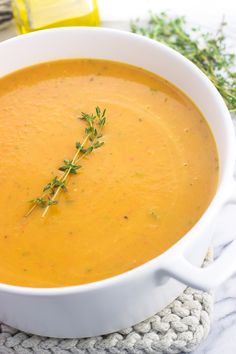 a white bowl filled with carrot soup and garnished with fresh thyerop