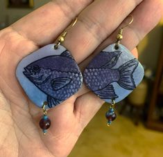 This is a nice pair of Artisan Enamel 'Fish' Pierced Earrings with gold-tone ear wires and crystal dangles. Handcrafted by Florida Enamel Artist Kathleen Wilcox, they measure 2.5 inches long including the hook and 1 inch wide. There is no scratch or scrape on the edges of the earring. That is only the photo. They are hand signed by the artist on the back of one of the earrings. Kathleen is an award winning artist based in Tallahassee Florida. She is known for her intricate designs of the flora a Blue Fish Hook Earrings For Gift, Gift Blue Fish Hook Earrings, Blue Fish-shaped Earrings For Gift, Shrinky Dink Earrings, Smoky Blue, Studio Artist, Tallahassee Florida, Shrinky Dink, Blue Lavender