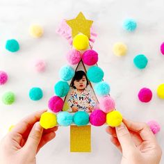 two hands holding up a photo frame with pom - poms around it