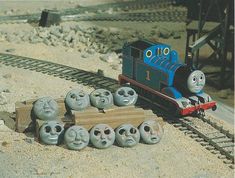 a toy train with many faces sitting on the tracks next to it's track