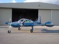 a small blue airplane parked in front of a hangar