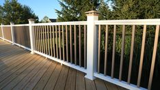 a wooden deck with white railings and trees in the background