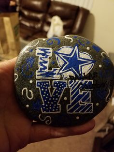 a hand holding a rock with the word love painted on it in blue and white