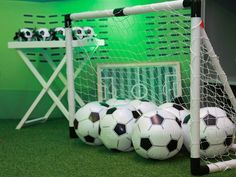 several soccer balls sitting on the ground next to a goalie's net in a green room