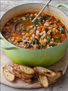 a green pot filled with soup next to sliced bread