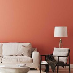 a living room with two white couches and a table in front of an orange wall