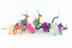 small plastic toy dinosaurs with colorful tulle skirts and unicorn hats on their heads are lined up against a white background