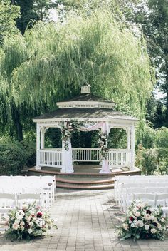 a gazebo surrounded by white chairs and flowers