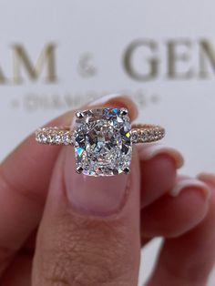 a close up of a person holding a ring with a cushion cut diamond on it