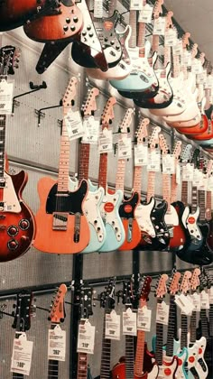 many guitars are hanging on the wall in a store with price tags attached to them