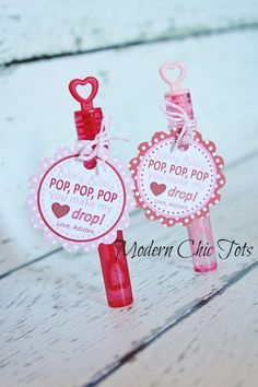 two red and pink wine bottle tags with hearts on them sitting on a wooden table