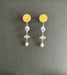 a pair of blue and white earrings on a black surface with a yellow disc in the background