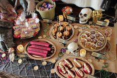 a table topped with lots of desserts and candles next to a skull head on top of a table