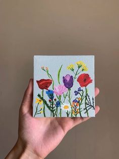 a hand holding up a small painting with flowers on it