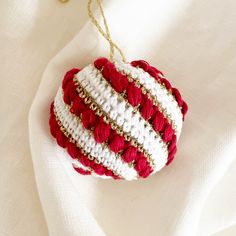 a red and white ornament hanging from a gold chain on a white cloth