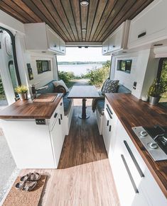 the interior of a camper with wood flooring and white cabinets, along with an open kitchen area