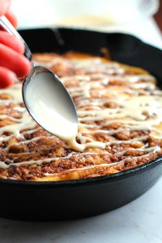 a person spoons milk from a skillet filled with cinnamon roll casserole