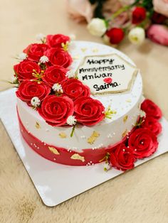 a white cake with red roses on top and happy anniversary written on the side next to it