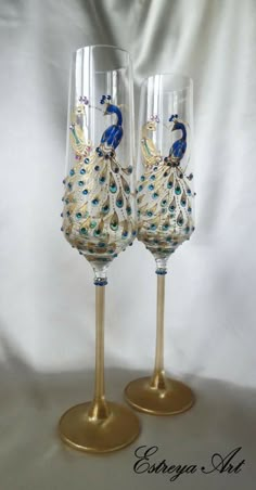 two wine glasses decorated with blue and gold peacocks are sitting side by side on a white background