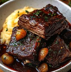 a bowl filled with meat, potatoes and gravy on top of a wooden table