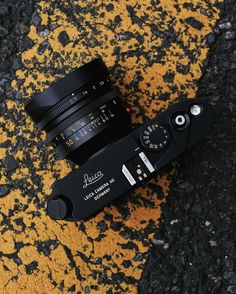 a black camera sitting on top of a yellow and black street curb next to asphalt