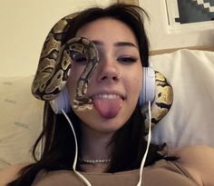 a woman with headphones and a snake wrapped around her face, making a funny face