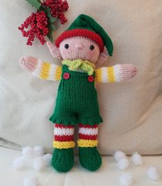 a knitted elf doll holding a red flower in its hand on a white pillow