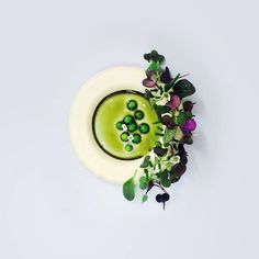 a white plate topped with green food next to purple flowers and leaves on top of it