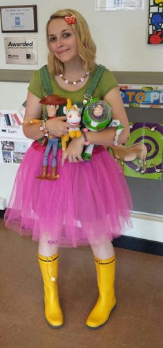 a woman wearing yellow rubber boots and a pink tutu skirt holding dolls in her hands