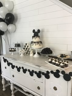 a mickey mouse cake and cupcakes on a buffet table with black and white balloons