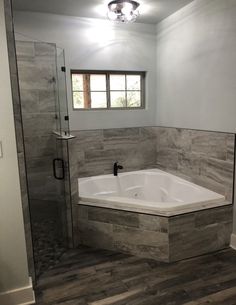 a bathroom with a walk in shower next to a white tub and wooden flooring