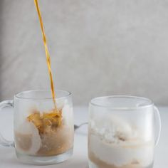 a person pours liquid from a bottle into two glass mugs