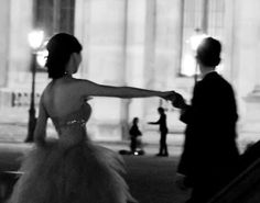 black and white photograph of a woman in a ball gown walking down the street with her arm outstretched