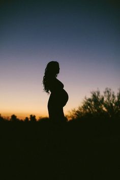 a pregnant woman is silhouetted against the evening sky with her hands on her hips