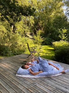 two people laying on a blanket in the middle of a wooden deck with chairs and trees