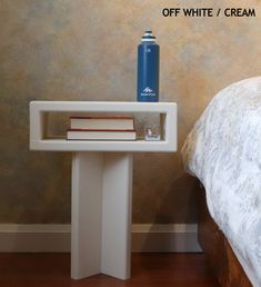 a white table with books on it next to a bed and a blue water bottle