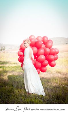 a woman in a white dress holding red balloons