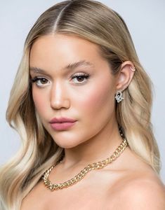 a woman with blonde hair wearing a gold necklace and matching earring is looking at the camera