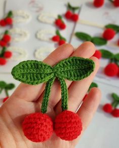 crocheted cherries in the shape of leaves and berries are being held by someone's hand