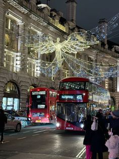 a double decker bus driving down a street next to tall buildings covered in christmas lights