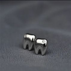 two silver tooth shaped earrings sitting on top of a black cloth covered bed sheet with a diamond in the middle