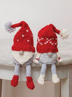 two knitted gnomes are hanging from a white table and one is wearing a red hat