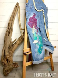 an old pair of jeans with mermaids painted on them sitting next to a tree branch