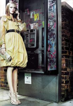 a woman in a yellow dress is standing next to a payphone and talking on the phone