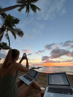 a woman sitting on the beach with her laptop and cell phone in front of her