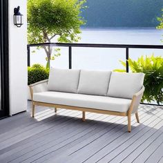 a white couch sitting on top of a wooden deck next to a tree and water