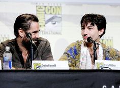 two men sitting at a table with microphones in front of them and one man wearing a scarf around his neck